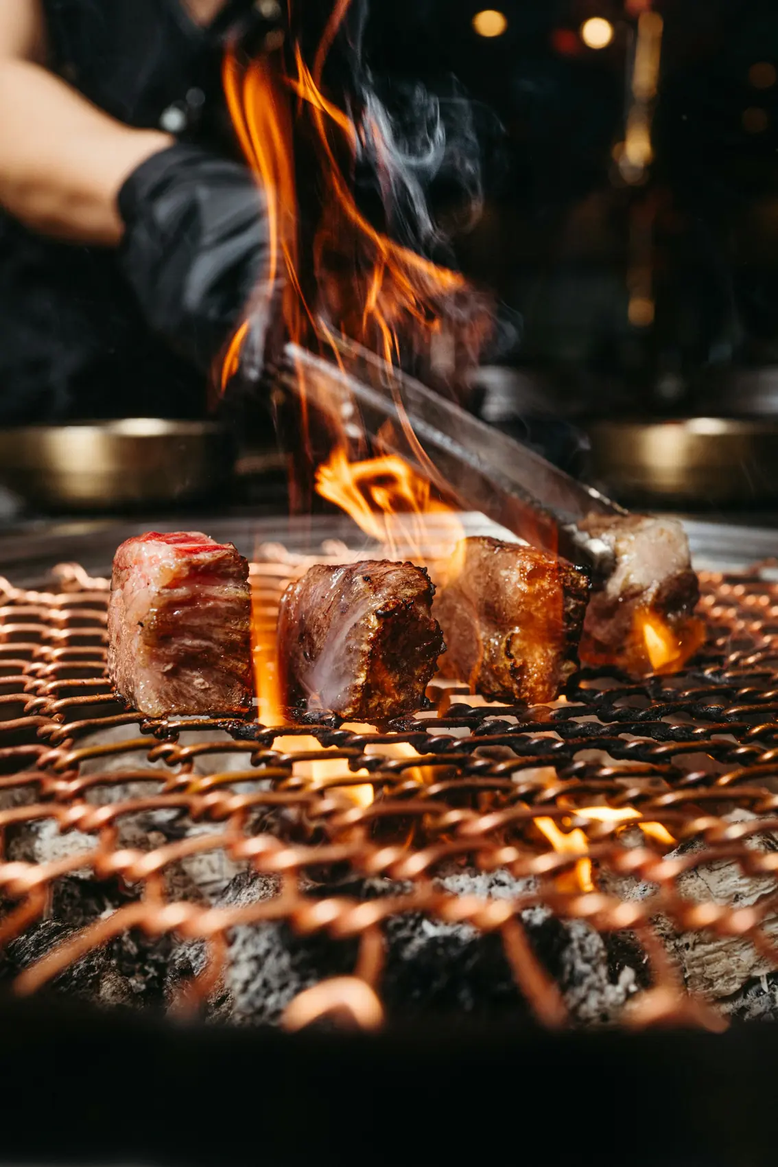 Am Holzkohlegrill: Hände mit Grillzange über der Flamme