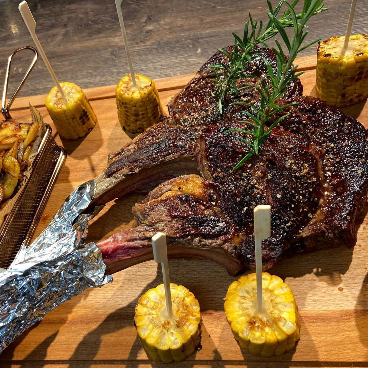 Steak am Knochen auf dem Holzbrett mit Maiskolben und Rosmarin